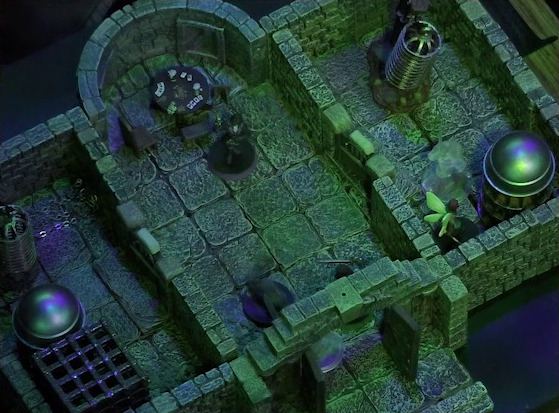 A battlemap of a stone aviary split into three rooms. Julien and Occtis’s undead monitor lizard stand in the open door to the main chamber, facing off against a ghost. Occtis stands further into the chamber in front of a circular table with a card game abandoned on it. Thimble is in a room to the right of the main chamber in front of a large cylindrical silvery metal cage, with another ghost to her left. To the left of the main chamber is a closed door leading to a room with a large cubic black metal cage, a large cylindrical silvery metal cage, and a large cylindrical metal hanging cage resembling a bird cage. To the right of the main chamber is a closed door leading to a room with the same kind of silvery metal cage, with Thimble in front of it, and hanging cage, although there is no large cubic cage.