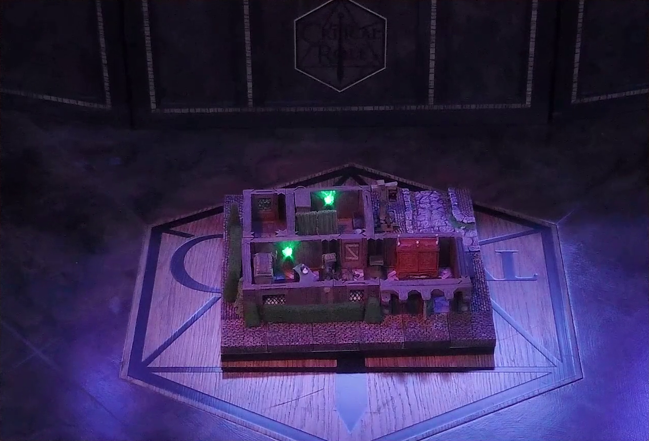 A battlemap of a street-side tailor shop eerily tinted purple and lit by glowing green torches. Kattigan and Wulferic stand in a main entry room in front of a curved front desk. A wardrobe is behind the desk and another one painted red is on the other side of the room. A door leads from the room to an adjoining one with curtains dividing it partially down the center. A third room is off to the side without a clear connection to the rest of the building.