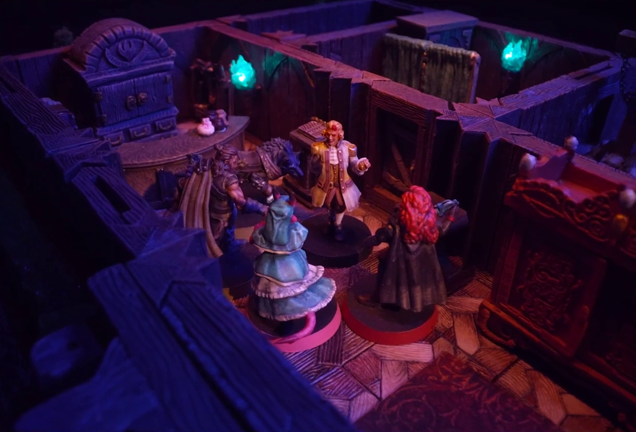 A battlemap of a street-side tailor shop eerily tinted purple and lit by glowing green torches. Kattigan, Wulferic, Tyranny, Bolaire, and Calastro Mercanaud stand in a main entry room in front of a curved front desk. A wardrobe is behind the desk and another one painted red is on the other side of the room. A door leads from the room to an adjoining one with curtains dividing it partially down the center. A third room is off to the side without a clear connection to the rest of the building.