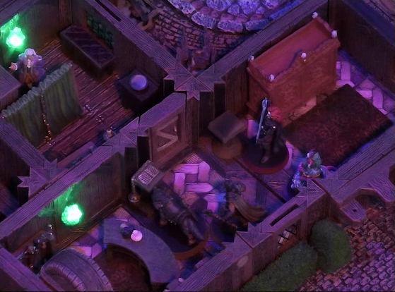 A battlemap of a street-side tailor shop eerily tinted purple and lit by glowing green torches. Kattigan, Wulferic, Tyranny, and Bolaire stand in a main entry room in front of a curved front desk. Calastro Mercanaud hides behind dividing curtains in an adjoining room. A wardrobe is behind the desk and another one painted red is on the other side of the room.