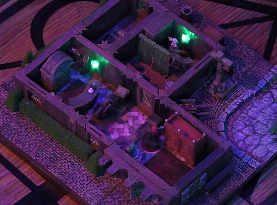 A battlemap of a street-side tailor shop eerily tinted purple and lit by glowing green torches. Wulferic, Tyranny, and Bolaire stand in a main entry room in front of a curved front desk. Kattigan faces off against Calastro Mercanaud behind dividing curtains in an adjoining room. A wardrobe is behind the desk and another one painted red is on the other side of the room. A third room is off to the side without a clear connection to the rest of the building. This room has stairs leading below ground. Outside the building is a wheelbarrow.