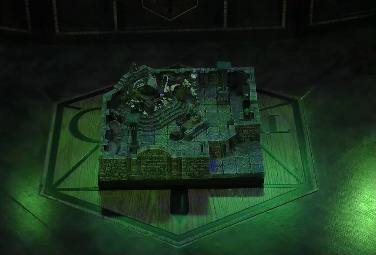 A battlemap of a stone crypt with open wooden coffins on one wall and a silvery metal iron maiden on another wall. Teor and Talcydimir lay downed next to a wooden table on which an undead Raimond Davinos is standing. A hoard of zombies surrounds the table. The table sits on a raised part of the floor in front of a wall decorated with carved skull motifs. On a box in front of the table sits a tray bearing multiple surgical instruments. The room is lit by eerie glowing green torches.