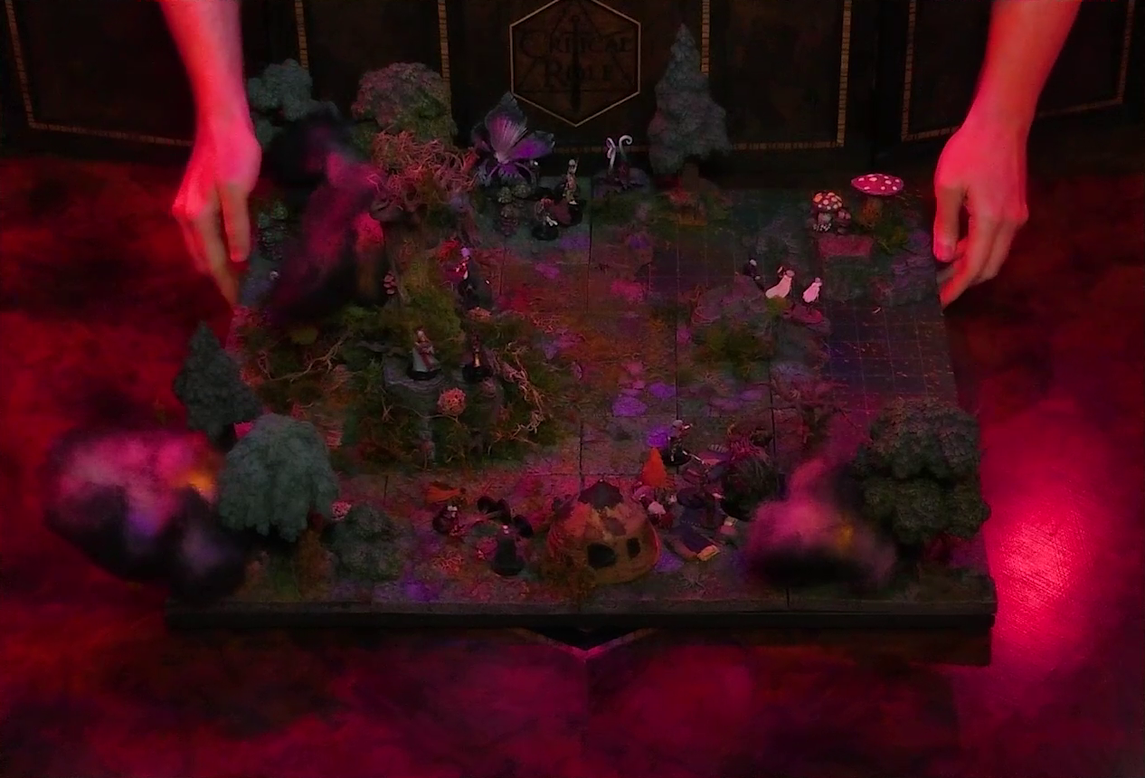 A battlemap of a forest clearing with a large leafless Hawthorn tree near the center. Fake smoke rises from that tree and others at the edges of the map. Orange lights indicate that the trees are on fire. A number of Candescent Creed members and fairy poachers are scattered around the area, especially at the base of the Hawthorn tree. A small animal hide hut is at the edge of the battlemap. Large red mushrooms with white spots and a huge purple flower are at the other end near a lake.
