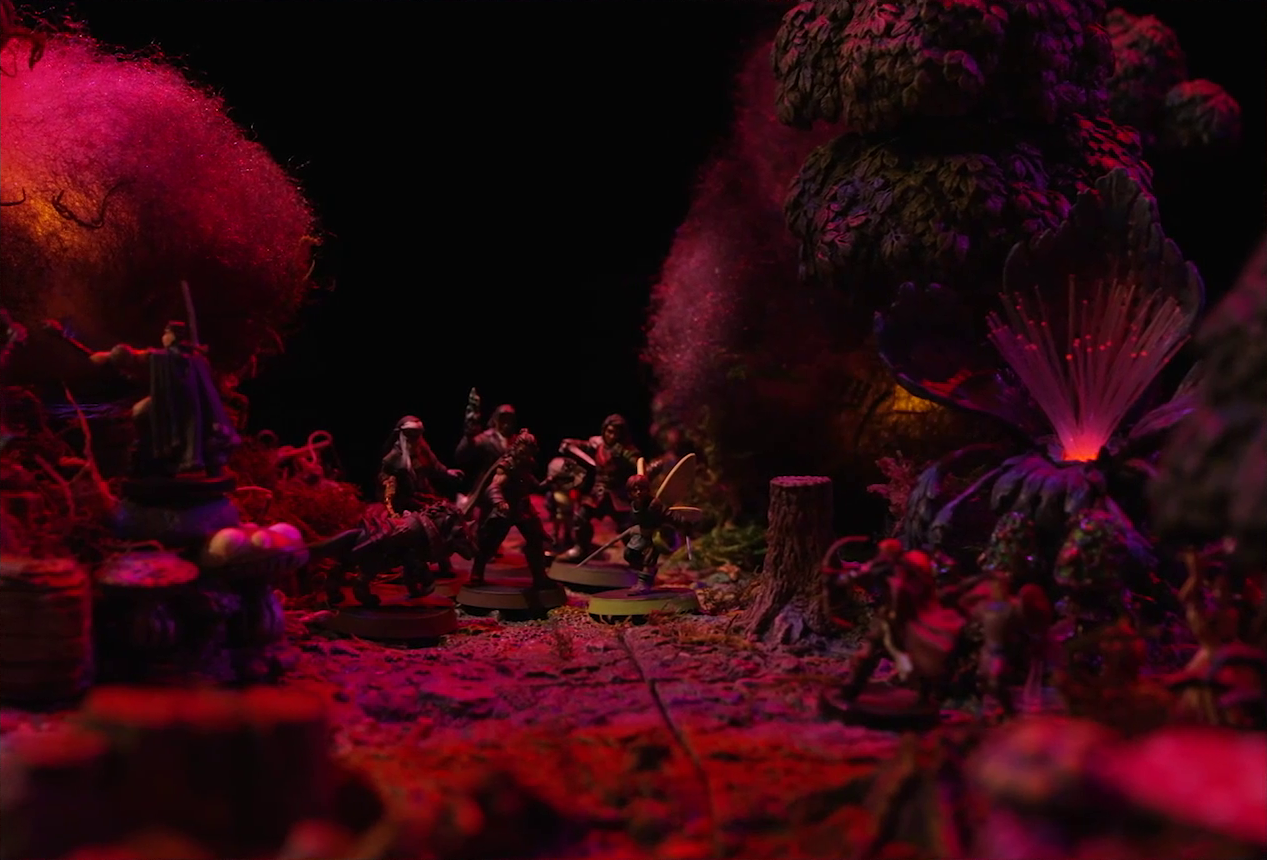 A battlemap of a forest clearing with a large leafless Hawthorn tree near the center, bathed in an eerie red glow. Fake smoke rises from that tree and others at the edges of the map. Orange lights indicate that the trees are on fire. Thimble, Kattigan, Wulferic, Vaelus, Occtis, Pin, and Ulbid Morn stand near the tree. A number of Candescent Creed members and fairy poachers are scattered around the area, especially at the base of the Hawthorn tree. A huge purple flower with long fibers emerging from it emits a red glow.