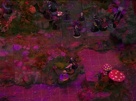 A battlemap of a forest clearing bathed in an eerie red glow. Kattigan, Wulferic, and Gaya Seremai face off against Candescent Creed members at the base of a large Hawthorn tree. Vaelus, Julien, and Ulbid Morn face off against enemies a short distance away. Three Candescent Creed members or fairy poachers stand by a lake. An island with large spotted mushrooms is in the lake, a very short distance from the shore. At the very edge of the image, Thimble faces off against a Candescent Creed member with a “DEAFENED” status ring around her miniature at the base of the Hawthorn tree.