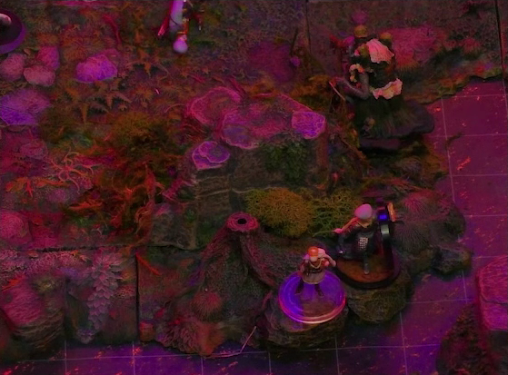 A battlemap of a forest clearing bathed in an eerie red glow. Two Candescent Creed members or fairy poachers stand at the edge of the lake. Nearby, Sallow the hag has just emerged from the lake and is facing inland.