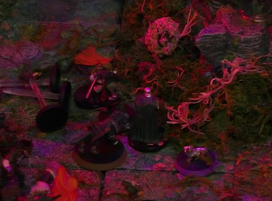 A battlemap of a forest clearing. Pin and Wulferic face off against two Candescent Creed members or fairy poachers at the base of a large Hawthorn tree. Three pixies lie downed near the combat.
