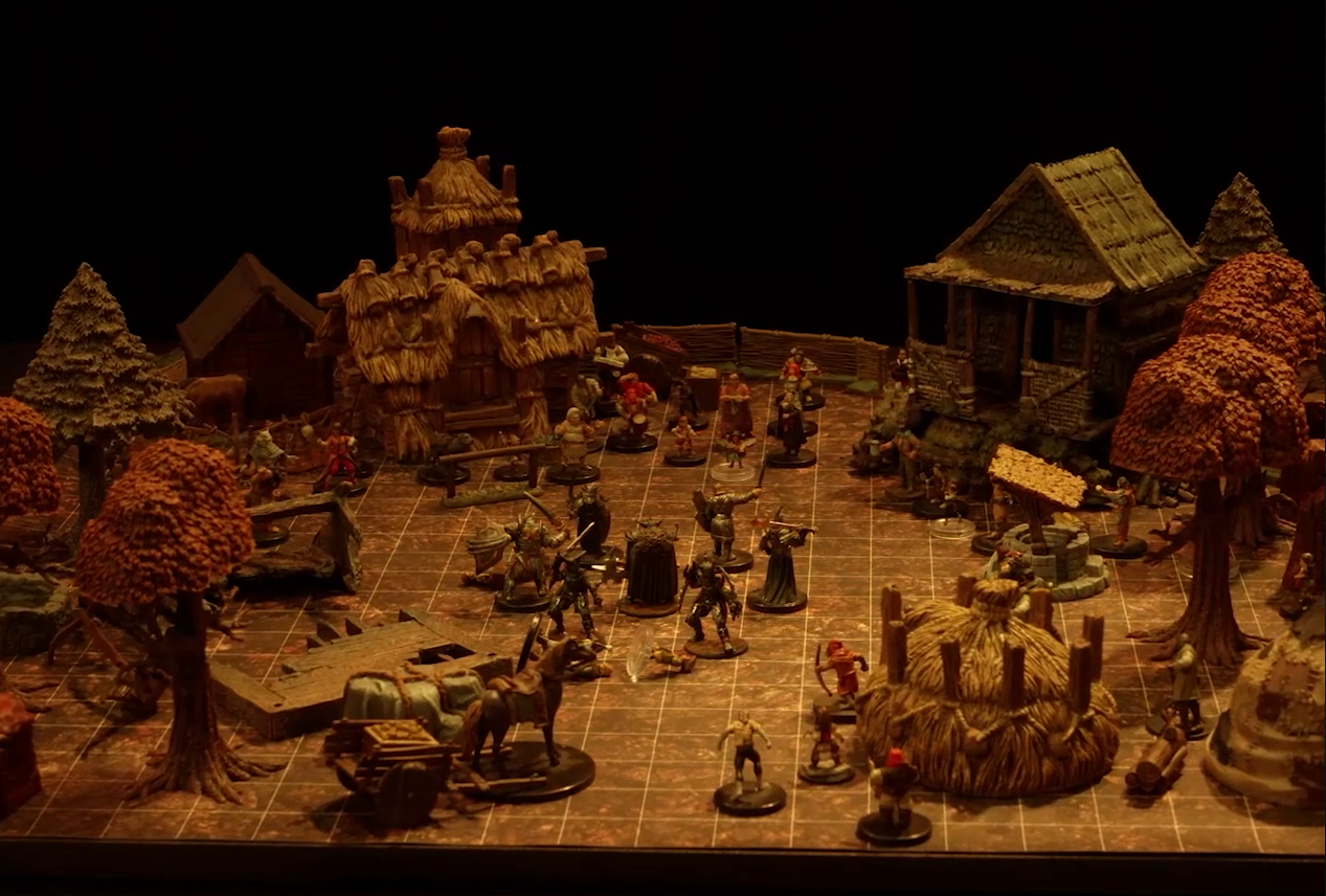 A battlemap of a small town square with a circle of black-armored soldiers surrounding a commander wearing a horned helmet. By the soldiers are three downed villagers. Surrounding the square are three small simple buildings made of wood and thatch, a collection of other villagers, trees in autumn colors, wooden debris, and a pile of hay.