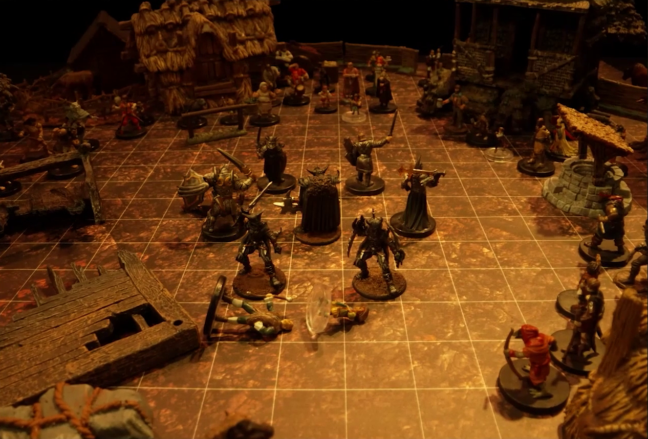 A battlemap of a small town square with a circle of black-armored soldiers surrounding a commander wearing a horned helmet. By the soldiers are three downed villagers. Surrounding the square are three small simple buildings made of wood and thatch, a collection of other villagers, trees in autumn colors, wooden debris, and a pile of hay.