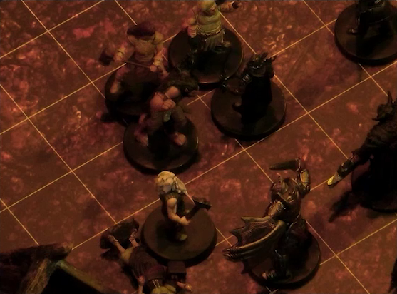 A battlemap focused on Garen and a group of three villagers facing off against four black-armored soldiers. One villager lays on the ground at Garen’s feet. Garen faces a soldier carrying a shield and dagger.