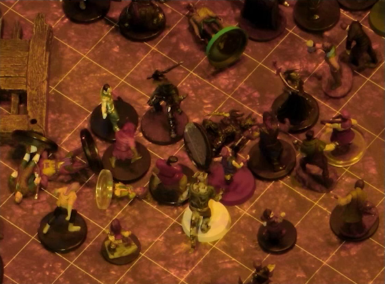 A battlemap focused on a fight between a group of black-armored soldiers and Fiedra, Crokas, and a number of villagers. Erro lays on the ground, with a number of villagers also downed. A soldier lays on the ground in front of Fiedra and Crokas.