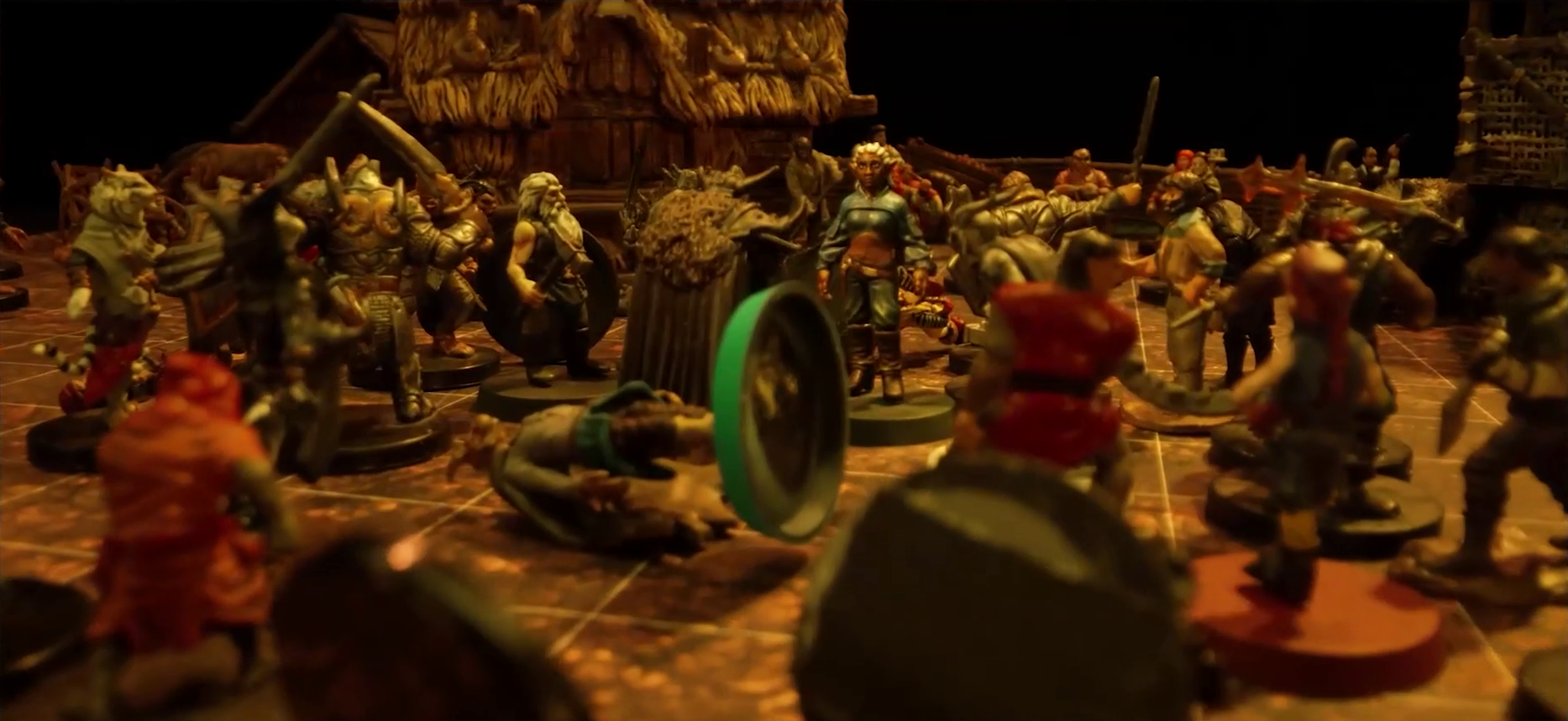A battlemap focused on Rei’nia in the midnst of a melee between her, Fiedra, Garen, and a number of villagers against a group of black-armored soldiers. Erro lays on the ground in the middle of the fight. Visible in the background are a couple simple buildings made of wood and thatch.