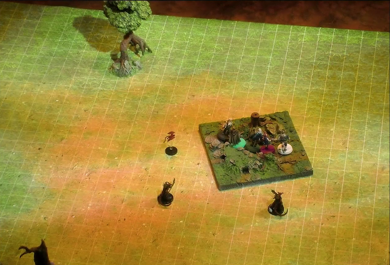 A battlemap of an open grassy plain, in the center of which on a textured map square are Garen, Erro, Rei’nia, Fiedra, and Crokas. Approaching them are two dragon-like devils armed with barbed pole weapons and a red flying impish creature. Two trees are visible in the otherwise empty plain.