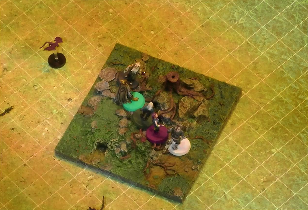 A battlemap of a grassy plain focused on a textured map square, on which are Garen, Erro, Rei’nia, Fiedra, and Crokas. Approaching them is a red flying impish creature. The map square is mostly covered in green, with some rocks and a single tree stump.