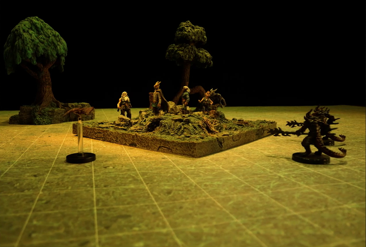 A battlemap of an open grassy plain focused on a textured map square, on which are Garen, Erro, Rei’nia, Fiedra, and Crokas. Approaching them are two dragon-like devils armed with barbed pole weapons and a red flying impish creature. Two trees are visible in the otherwise empty plain.