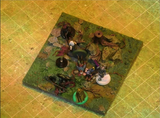A battlemap of a grassy plain focused on a textured map square, on which are Garen, Erro, Rei’nia, Fiedra, and Crokas facing off against two dragon-like devils and a red flying impish creature. Fiedra and Rei’nia are fallen, as is one devil. The devils are armed with barbed pole weapons. The map square is mostly covered in green, with some rocks and a single tree stump.