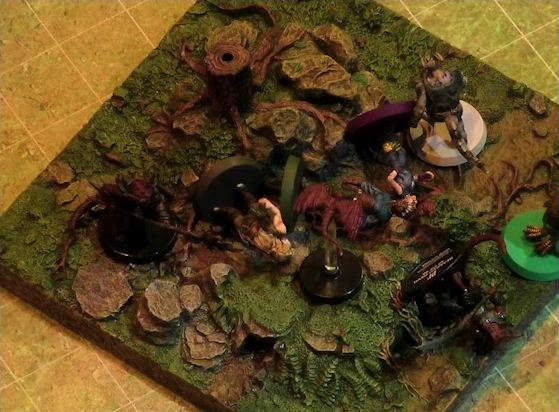 A battlemap of a grassy plain focused on a textured map square, on which are Garen, Erro, Rei’nia, Fiedra, and Crokas facing off against two dragon-like devils and a red flying impish creature. Garen, Fiedra, and Rei’nia are fallen, as is one devil. The devils are armed with barbed pole weapons. The map square is mostly covered in green, with some rocks and a single tree stump.