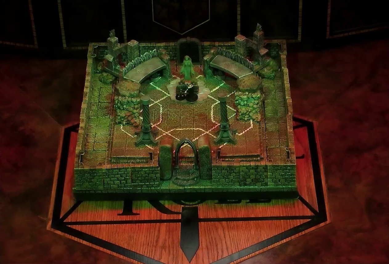 A battlemap of a stone temple interior. Lord Callister and Timothy stand before an altar and statue of the Moonweaver, which sits in front of a dark archway between two stone platforms. The statue stands on a bed of white crystal. The entrance to the room is also an archway, leading to two stone pillars. In the back corners of the room are grotesques placed on buttresses.
