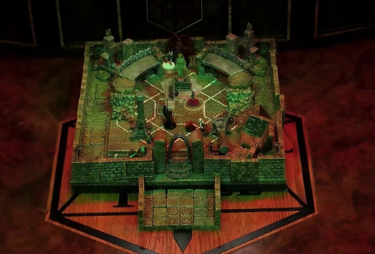 A battlemap of a stone temple interior. Admodeus stands, huge wings behind him, at the rear of the room behind a statue of the Moonweaver. Crokas levitates in the air. On the ground are Timothy, Lord Callister, Fiedra with a status ring, Erro, Garen, and a few devils and imps. Garen stands in front of a toppled stone pillar.