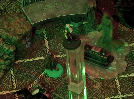 A battlemap of a stone temple interior. Garen levitates in the air in front of an altar and statue of the Moonweaver. Erro stands on the ground nearby in front of a dark devil with wide wings. On the altar is an open book.