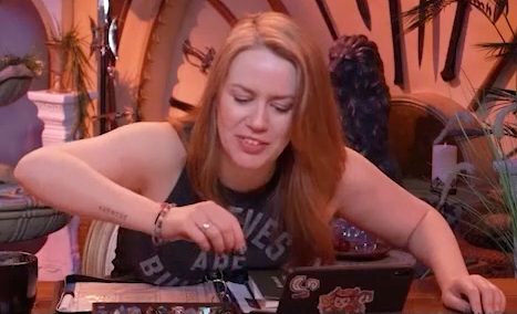 Marisha at the table, staring intently at a d20 in her hand to determine what she just rolled.
