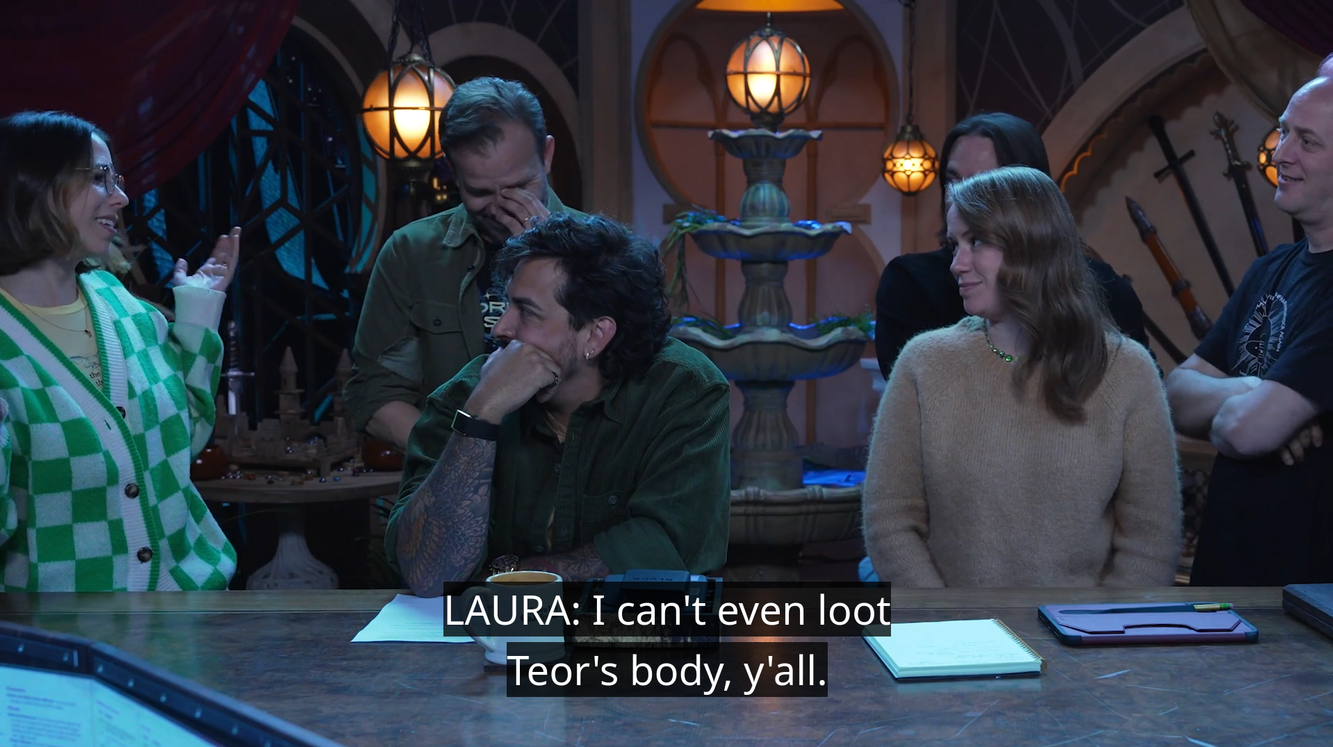 Laura at the table during the Cooldown saying “I can’t even loot Teor’s body, y’all.”. She shrugs, speaking to Liam, Robbie, Marisha, Matt, and Taliesin. Liam laughs with his face in his hand, while the others smile slightly.