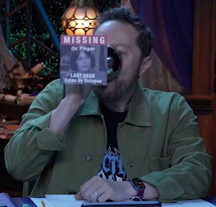 Sam drinking from a silver chalice with an image of Whitney pasted on the bottom. The text “MISSING” is above the image in white on a red background. Underneath it is written “Dr. Finger. LAST SEEN Eaten by Octopus”. The image of Whitney is black and white. She looks forward somberly. Sam tips the chalice fully horizontally into his mouth.