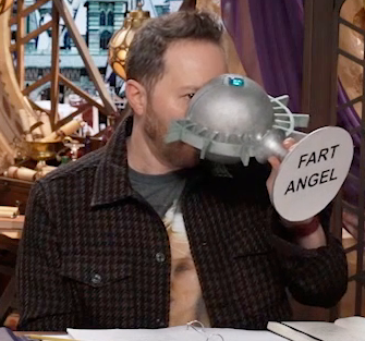 Sam drinking from a large ornate silver chalice with the text “FART ANGEL” printed on white paper pasted to the bottom. The text is in a block font. The chalice has spokes emerging from the curve of its cup reminiscent of Candescent Creed sun ray designs. A turquoise gem is set in the side, matching the gem in Wicander’s circlet. Sam tips the chalice horizontally into his mouth. His eye peeks out from behind the cup, looking forward.