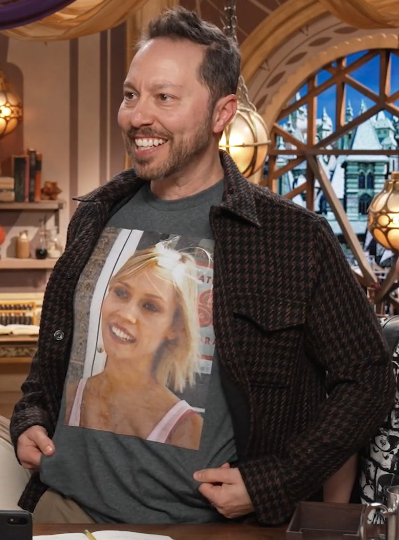 Sam standing behind the table, wearing a gray T-shirt with an image of a young Whitney on the front. She has blond hair, no visible piercings, and is wearing a pink tank top. The picture appears to have been taken in front of a storefront. Sam smiles, flattening out the shirt for better visibility.
