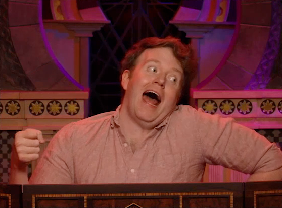 Brennan playing as Tsul’rekshi, making an unhinged face. He tilts his head back unnaturally, his eyes wide and mouth open. His right hand mimicks holding a staff.